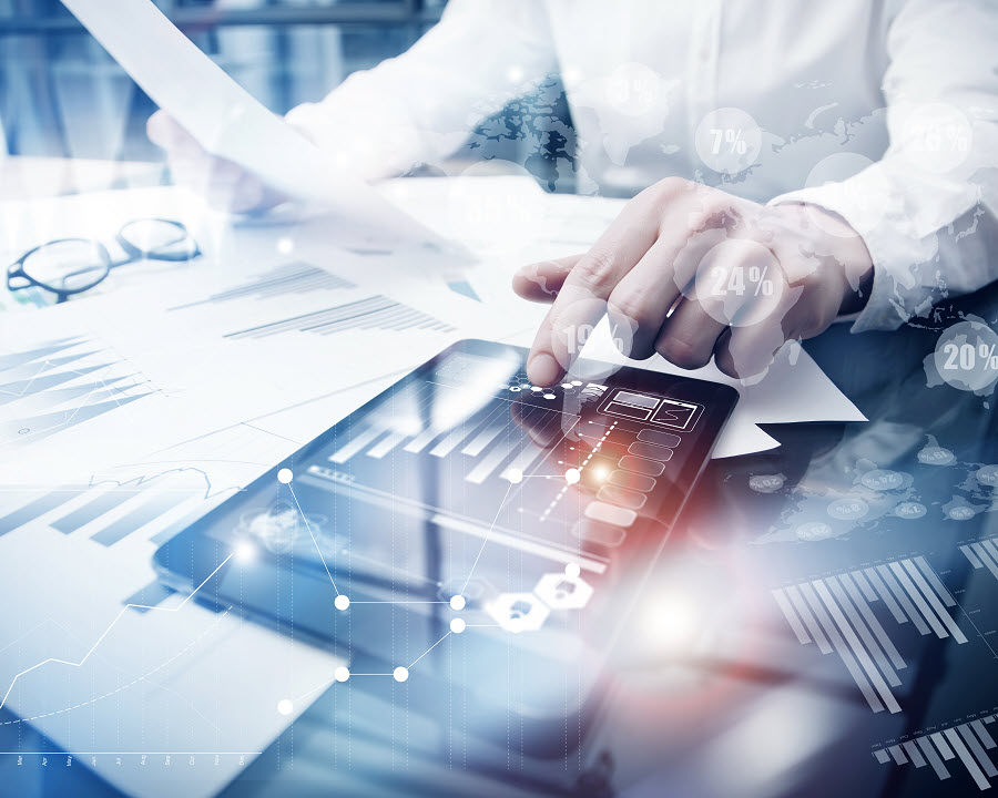 Business professional reviewing financial documents and using a tablet with charts and digital analytics overlays on a desk
